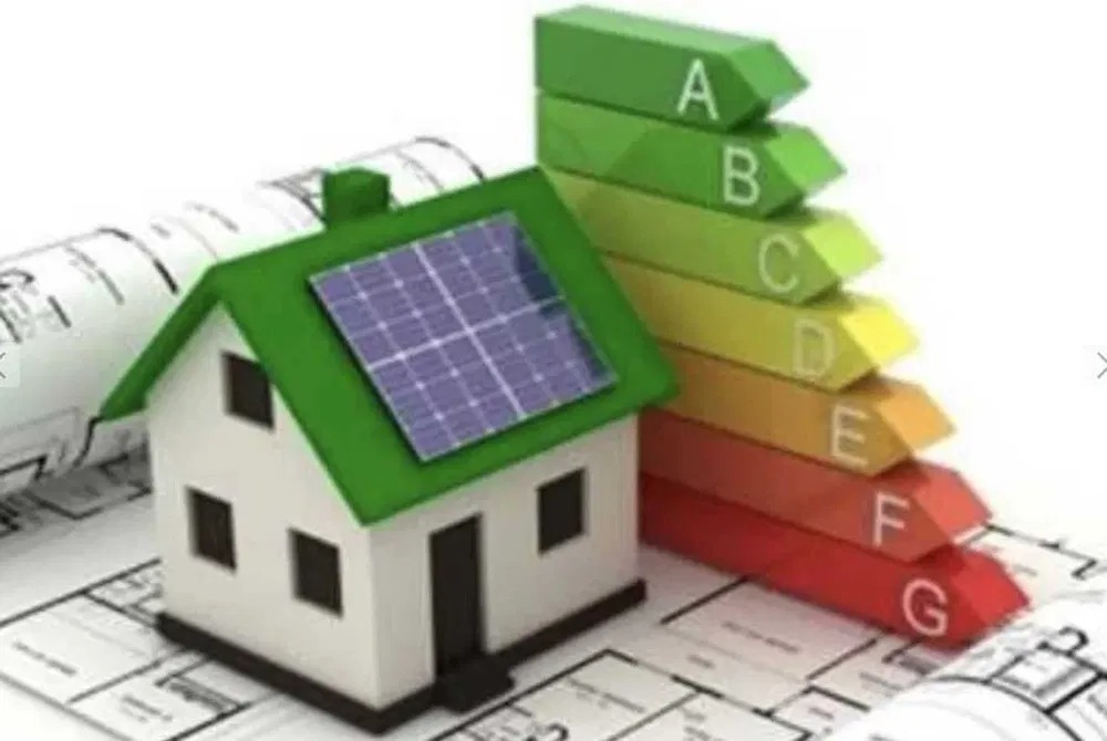 Model domu z panelami słonecznymi na dachu, obok skala efektywności energetycznej od A do G, leżący na planach architektonicznych.