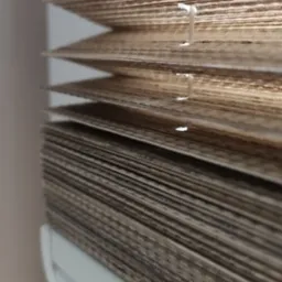 Detale zamkniętych, beżowo-brązowych żaluzji drewnianych, widoczne sznurki regulacyjne i biała rama okienna w tle.