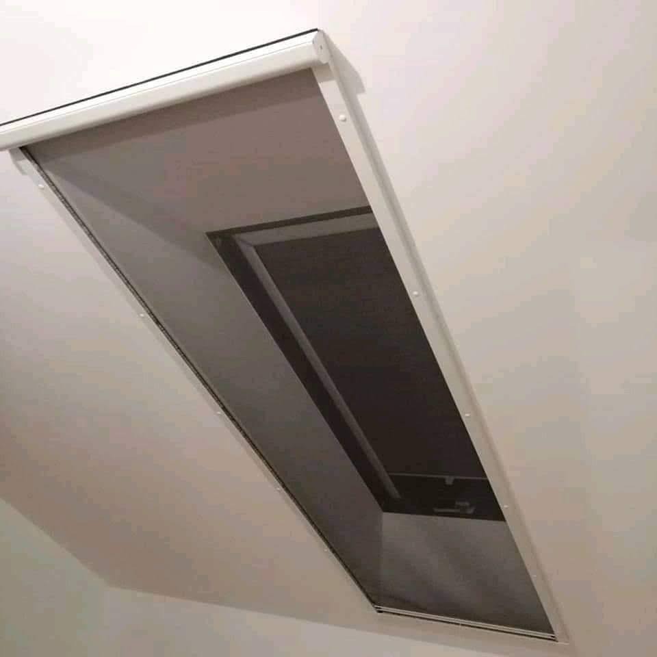 Zamknięta, biała roleta wewnętrzna zamontowana w oknie dachowym, widok od dołu, z widoczną konstrukcją rolety.