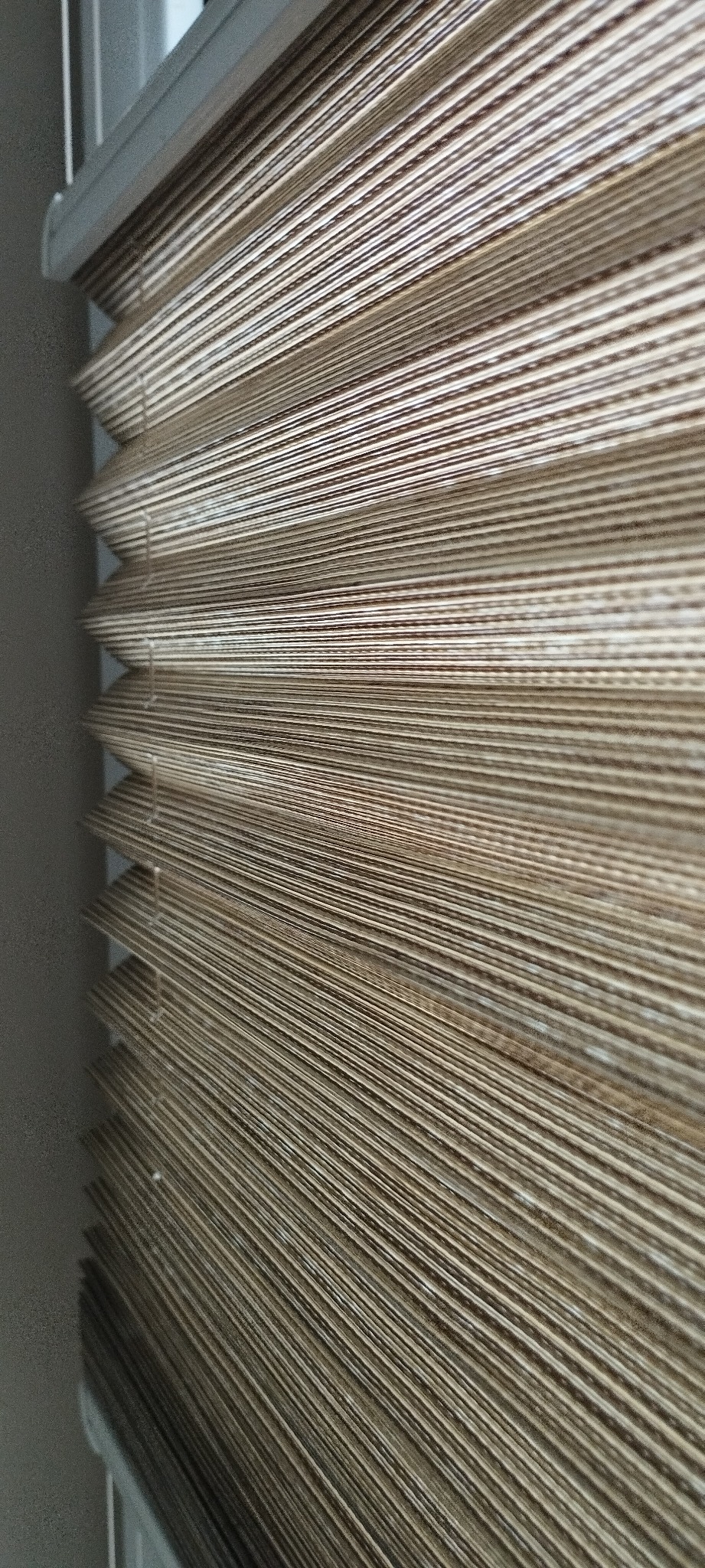 Beżowe, plisowane osłony okienne z widocznym systemem sznurkowym, częściowo zasłonięte, zbliżenie na fakturę materiału.