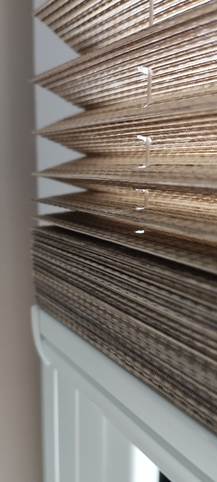 Detale zamkniętych, beżowo-brązowych żaluzji drewnianych, widoczne sznurki regulacyjne i biała rama okienna w tle.