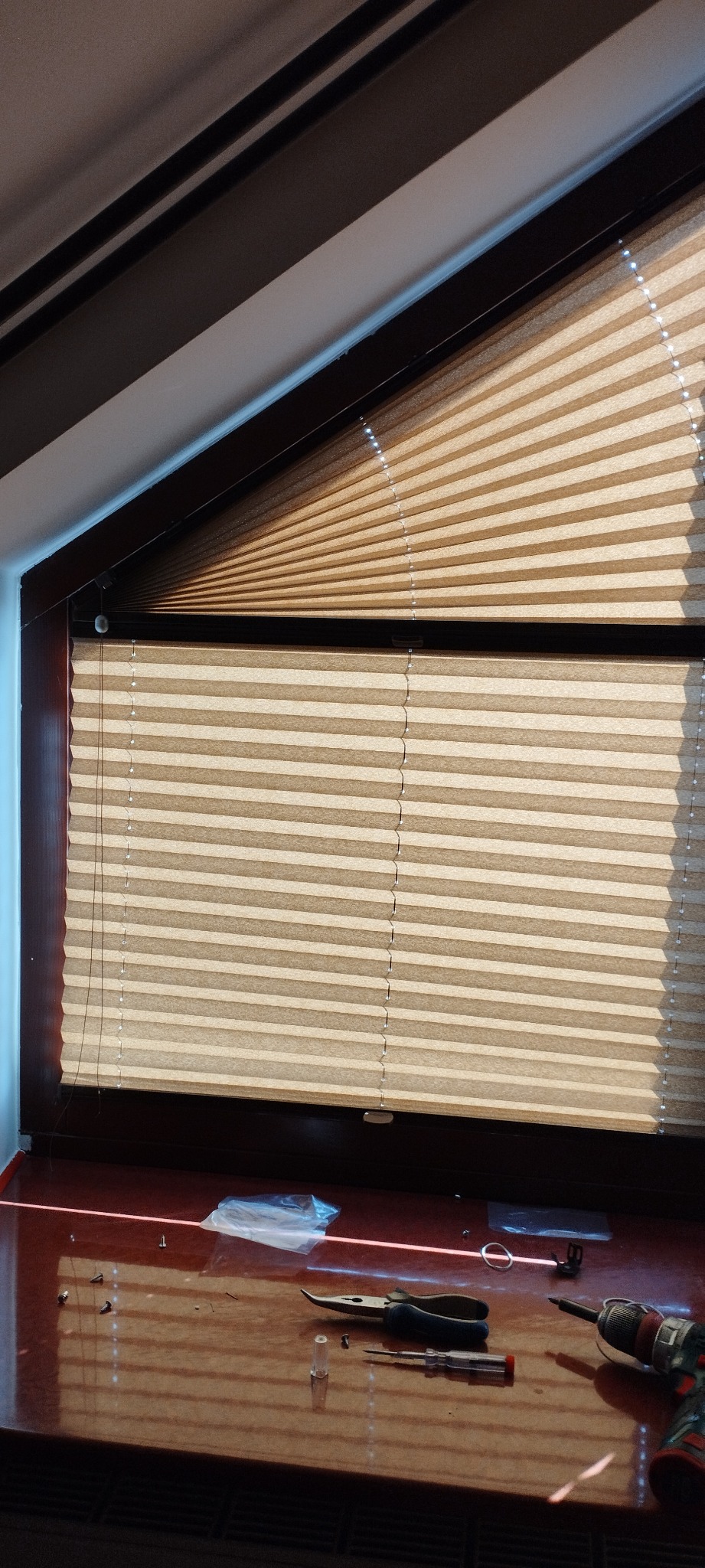 Beżowe plisy okienne zamontowane w oknie na poddaszu w Zgierzu, widoczne narzędzia i akcesoria do montażu na parapecie.