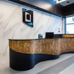 Recepcja z blatem imitującym rdzę, czarną podstawą i marmurową ścianą w tle, uzupełniona o logo firmy.