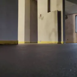 Świeżo wylana, ciemnoszara posadzka w surowym wnętrzu z widocznymi kolumnami i żółtą taśmą zabezpieczającą przy ścianach.