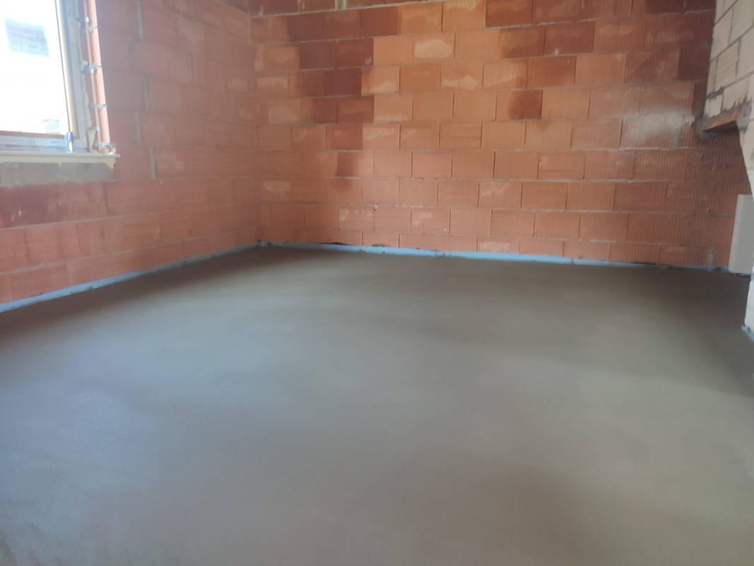 Świeżo wylana, gładka posadzka jastrychowa w surowym wnętrzu z ceglanymi ścianami i oknem po lewej stronie.