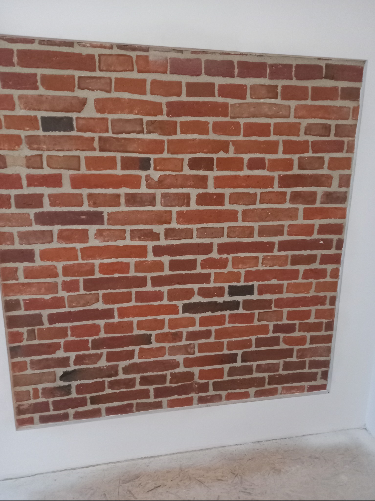 Fragment ściany z czerwonej cegły, ułożonej w regularny wzór, otoczony białą ramą z gładkiego tynku, widok z dołu.