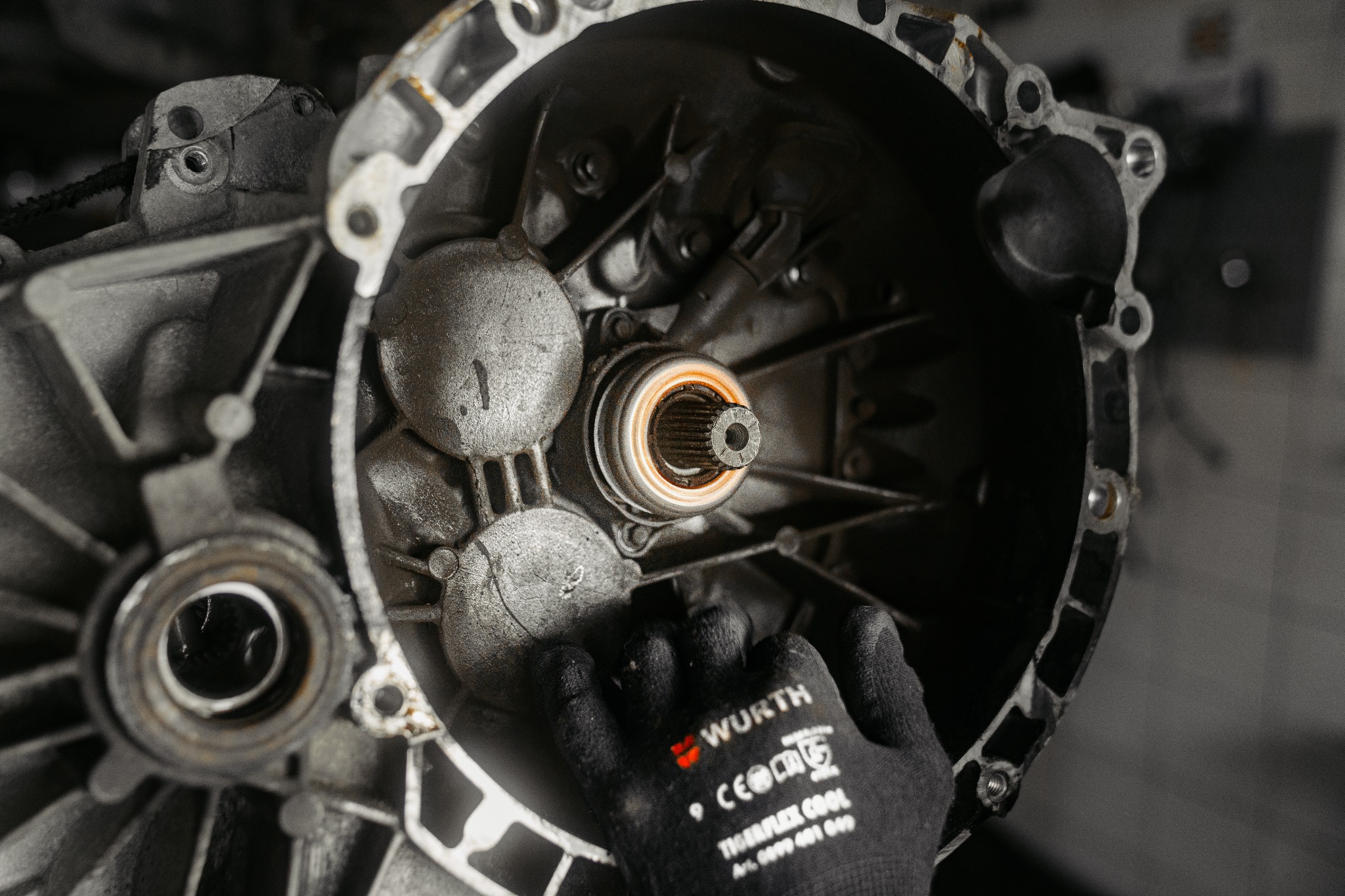 Otwarta skrzynia biegów samochodowa z widocznym wałkiem sprzęgłowym, manipulowana przez dłoń w czarnej rękawicy roboczej marki Wurth.