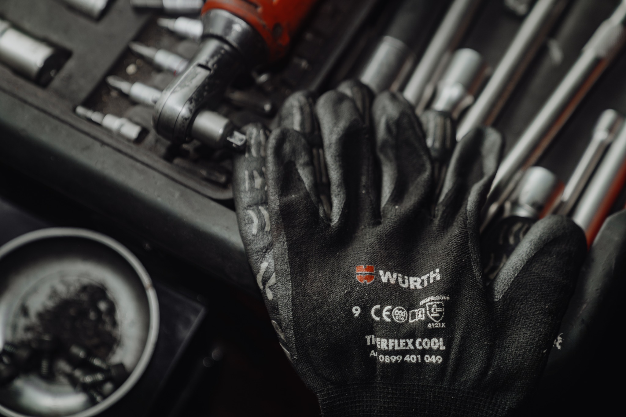 Rękawica robocza marki Wurth na tle skrzynki z narzędziami warsztatowymi, w tym klucze nasadowe i wkrętaki.