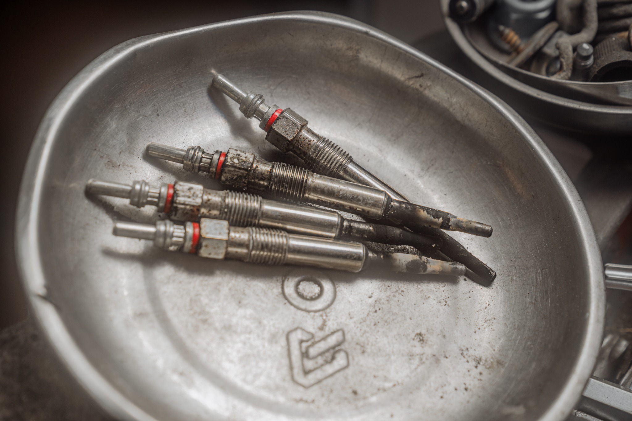 Używane, zabrudzone nagarem świece żarowe w metalowej misce warsztatowej, widoczne ślady eksploatacji.