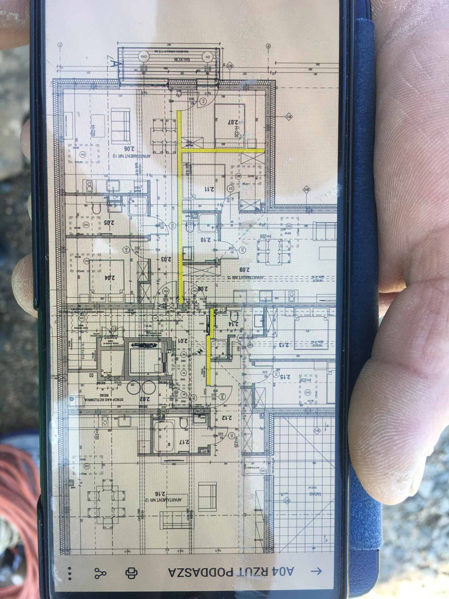 Rzut poddasza z zaznaczonymi zmianami na ekranie smartfona trzymanego w dłoni, widoczne elementy instalacji i wymiary pomieszczeń.