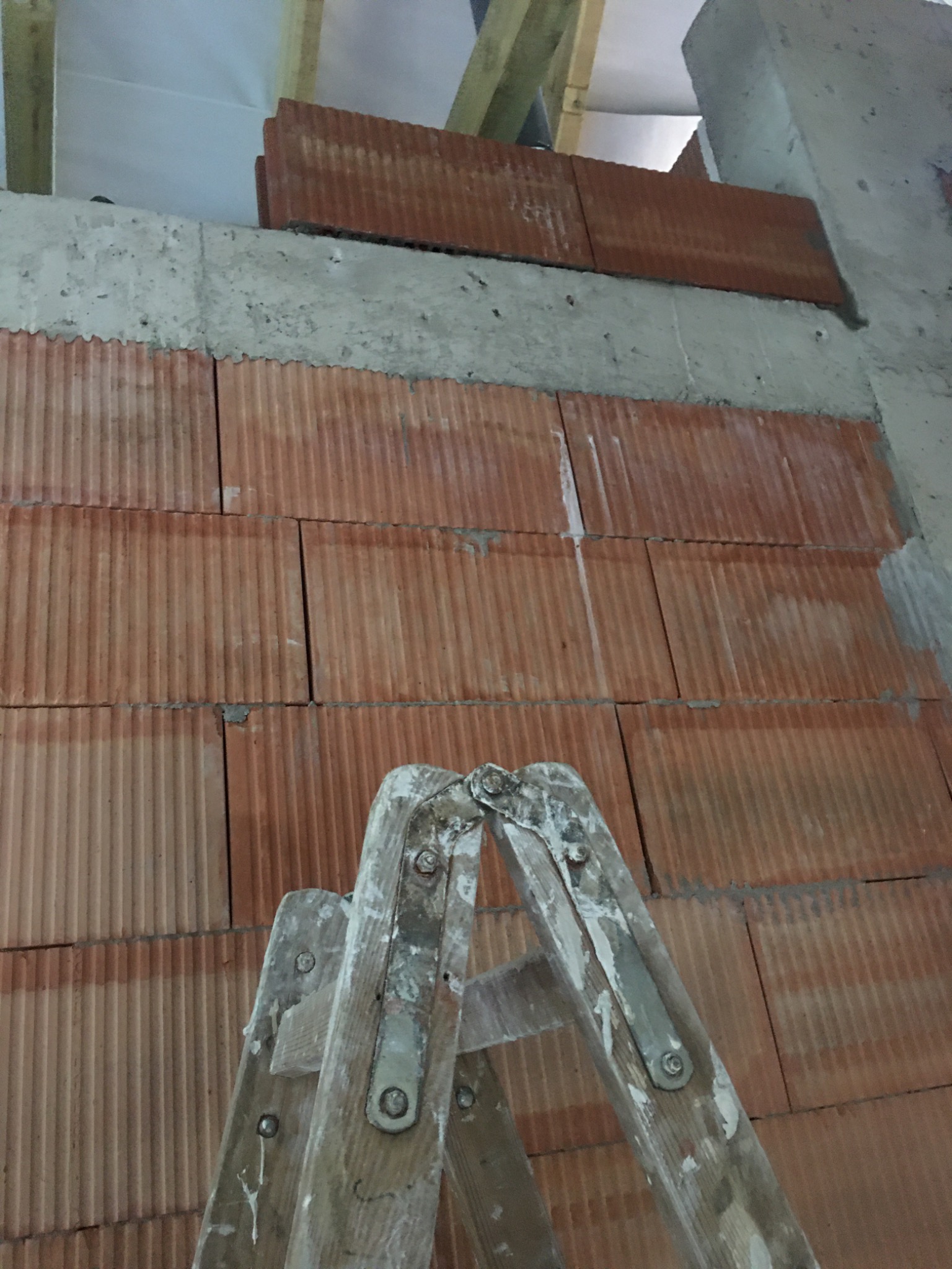 Wznoszenie ściany z cegły ceramicznej wewnątrz budynku, widoczna drabina malarska i fragment stropu betonowego.