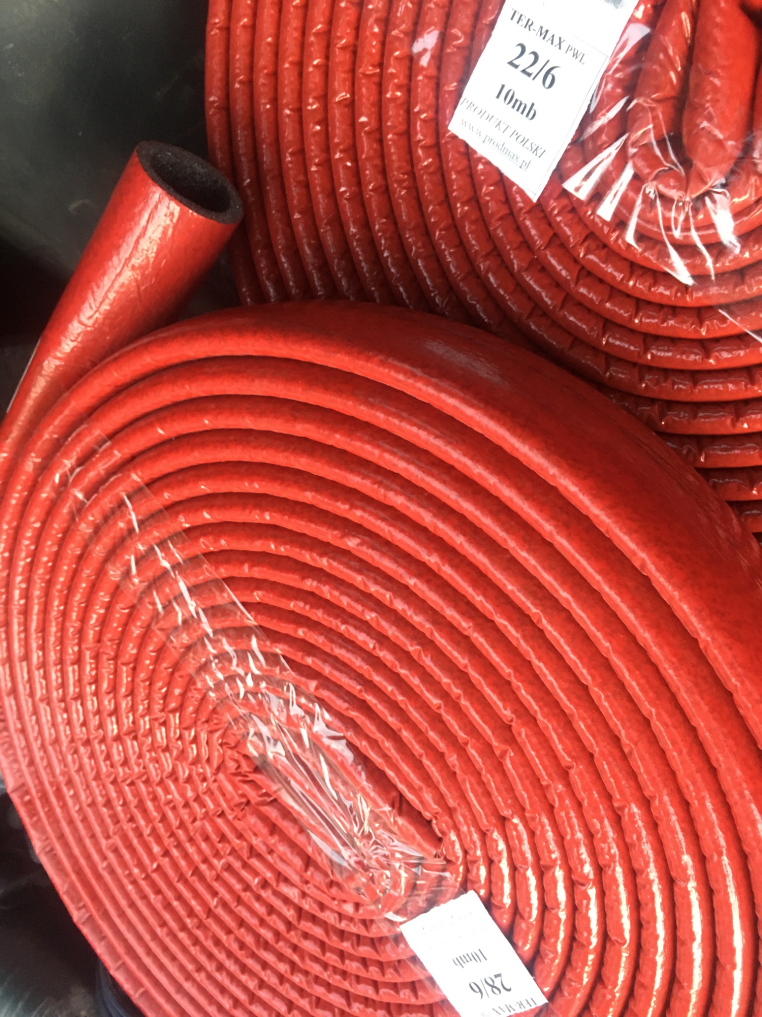 Zrolowane, czerwone rury izolacyjne z czarnym wnętrzem, owinięte folią, z etykietą 'TER-MAX PWL 22/6 10mb PRODUKT POLSKI'