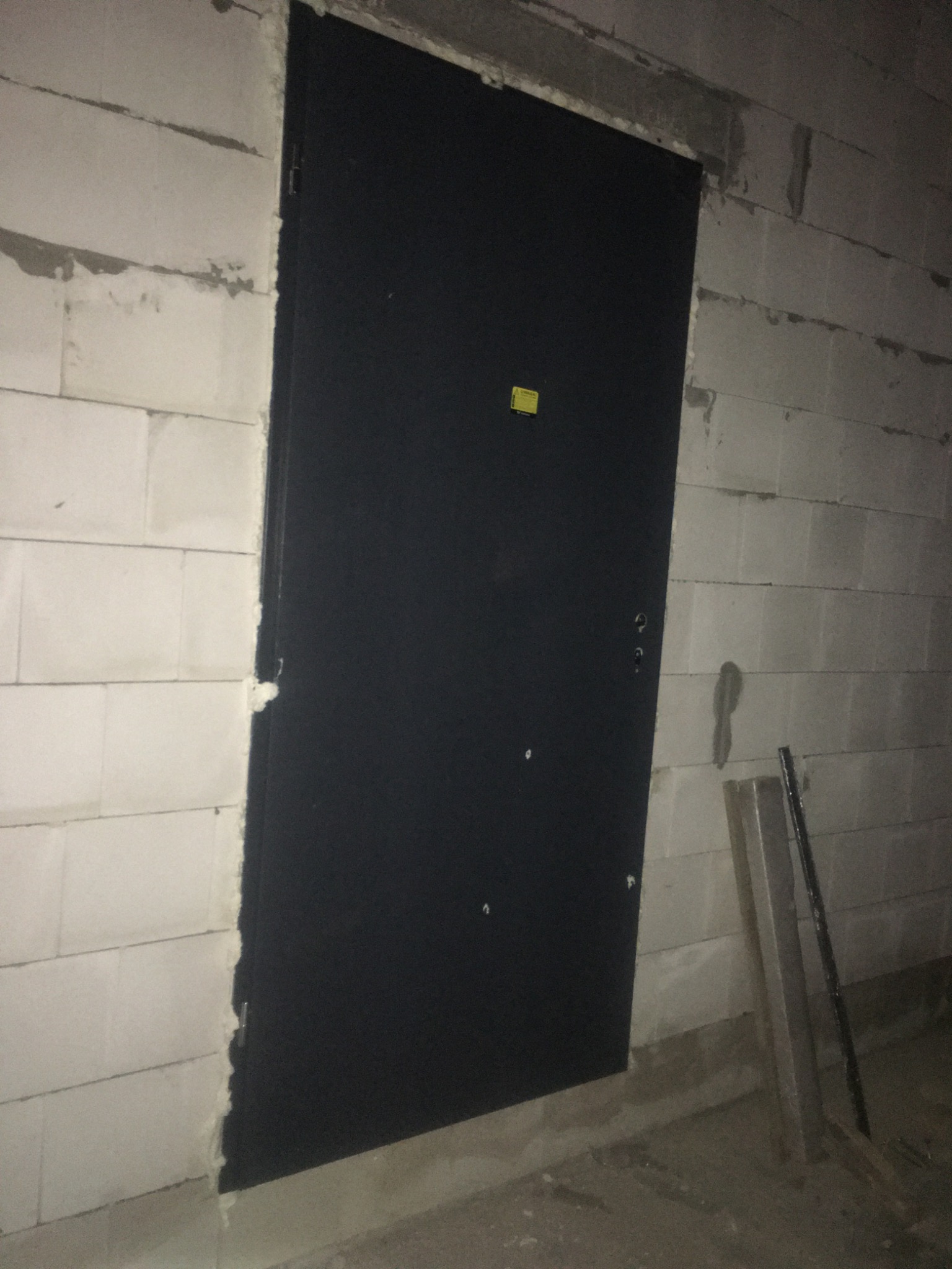 Czarna, metalowa, nowa brama antywłamaniowa zamontowana w surowym murze z betonu komórkowego, widoczne ślady zaprawy montażowej przy ościeżnicy.