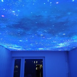 Fabryka Sufitów Yauheni Tratsiak - Pokój z efektem gwieździstego nieba na suficie. Błękitne oświetlenie podkreśla kosmiczny wzór. Widoczne drzwi i białe ściany.