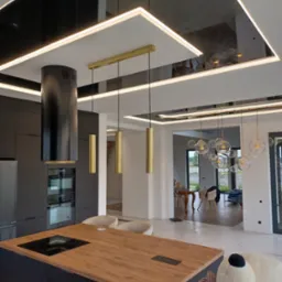 Nowoczesny salon z czarnym sufitem napinanym z oświetleniem LED, odbijającym detale wnętrza, w tym wyspę kuchenną i lampy wiszące.