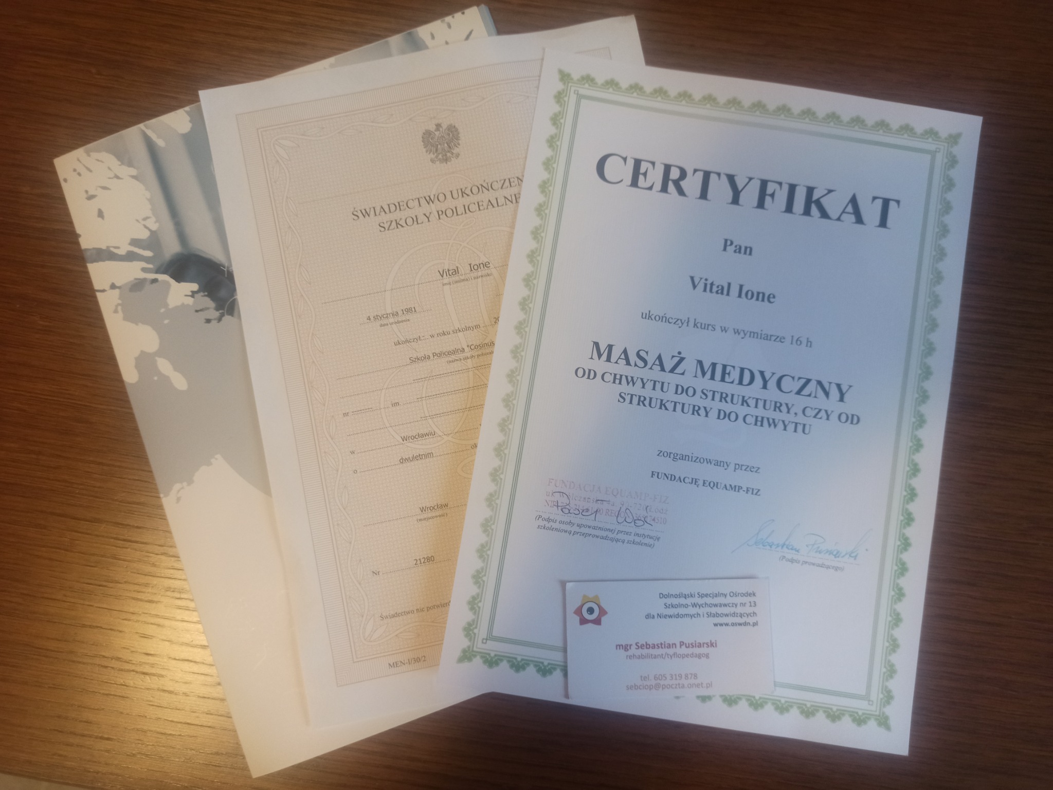 Świadectwo ukończenia szkoły policealnej i certyfikat ukończenia kursu masażu medycznego, leżące na drewnianym stole, obok wizytówki.