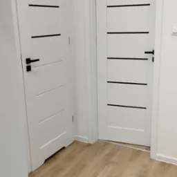 Dwie białe, nowoczesne drzwi z czarnymi, poziomymi paskami i klamkami na jasnej podłodze panelowej, widok z niskiego kąta.