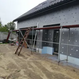 Dom jednorodzinny w trakcie ocieplania elewacji styropianem grafitowym, widoczne rusztowanie i drabina oparta o ścianę.