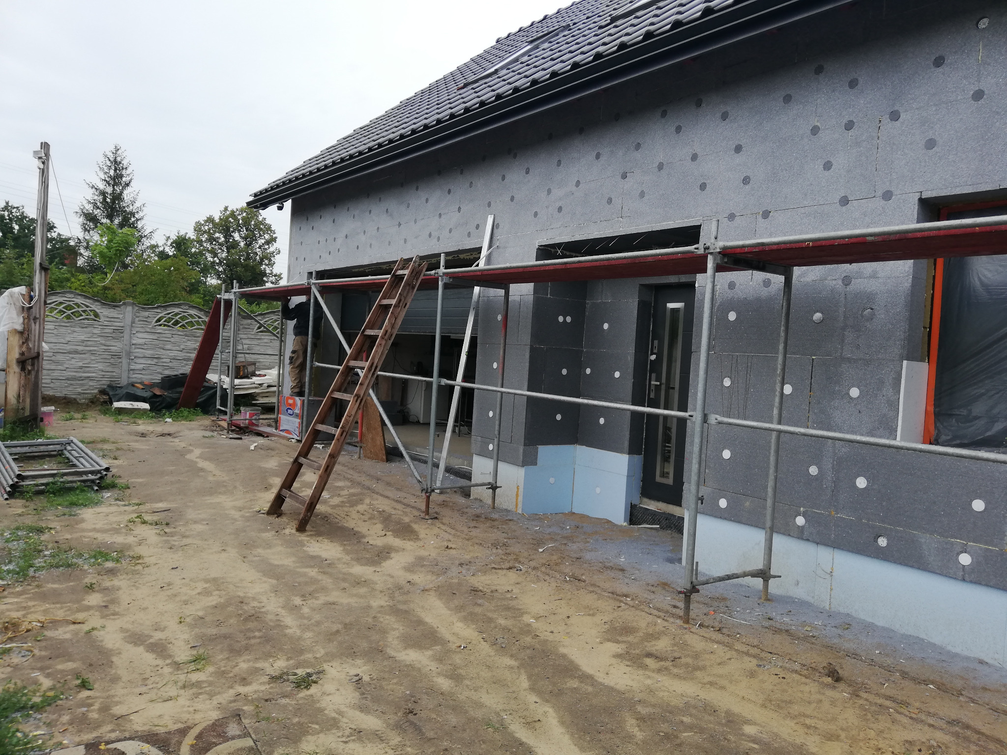 Dom jednorodzinny w trakcie ocieplania elewacji styropianem grafitowym, widoczne rusztowanie i drabina oparta o ścianę.