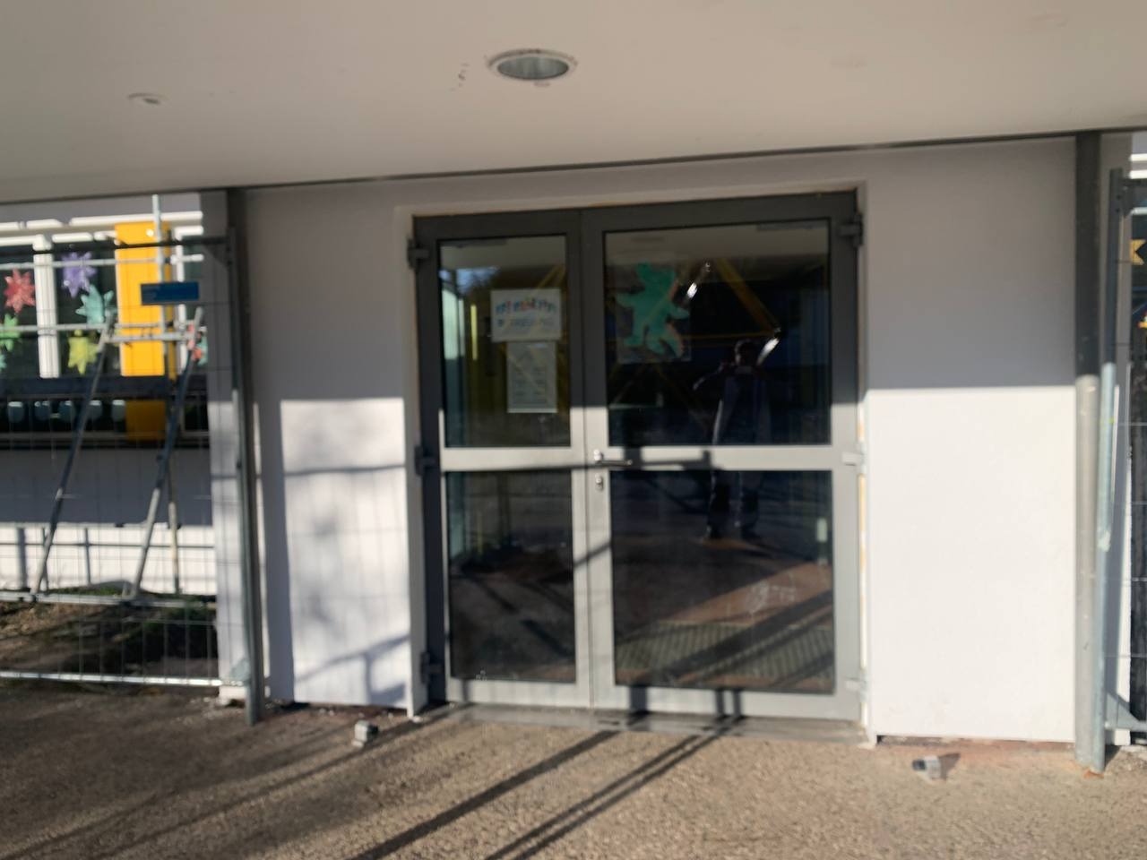 Wejście do budynku z nową, białą elewacją; widoczne metalowe rusztowanie i dekoracje okienne.