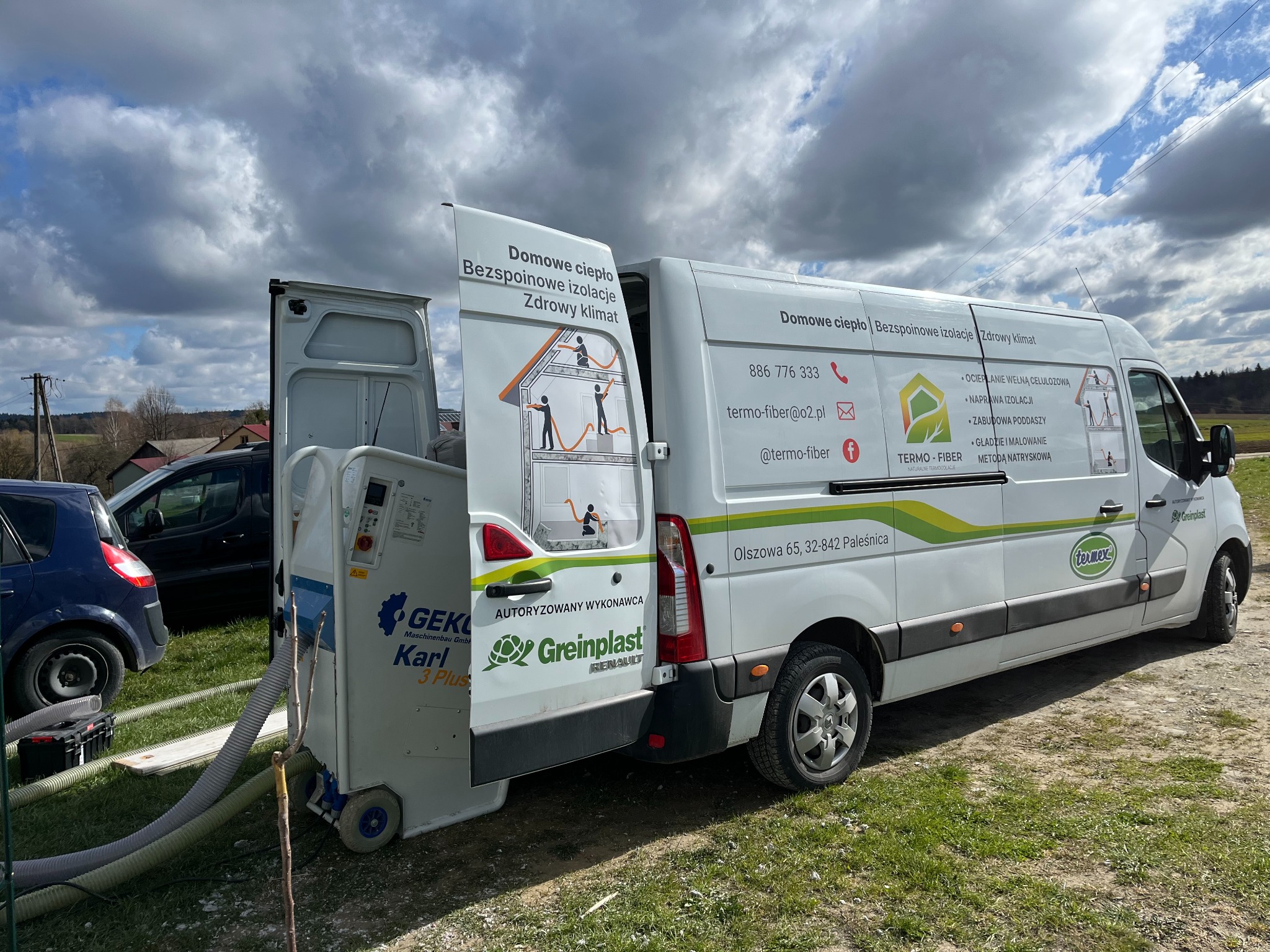 Mobilny agregat do ociepleń celulozą Geko Karl 3 Plus obok białego busa z reklamą termoizolacji natryskowej, na tle pochmurnego nieba i zieleni.
