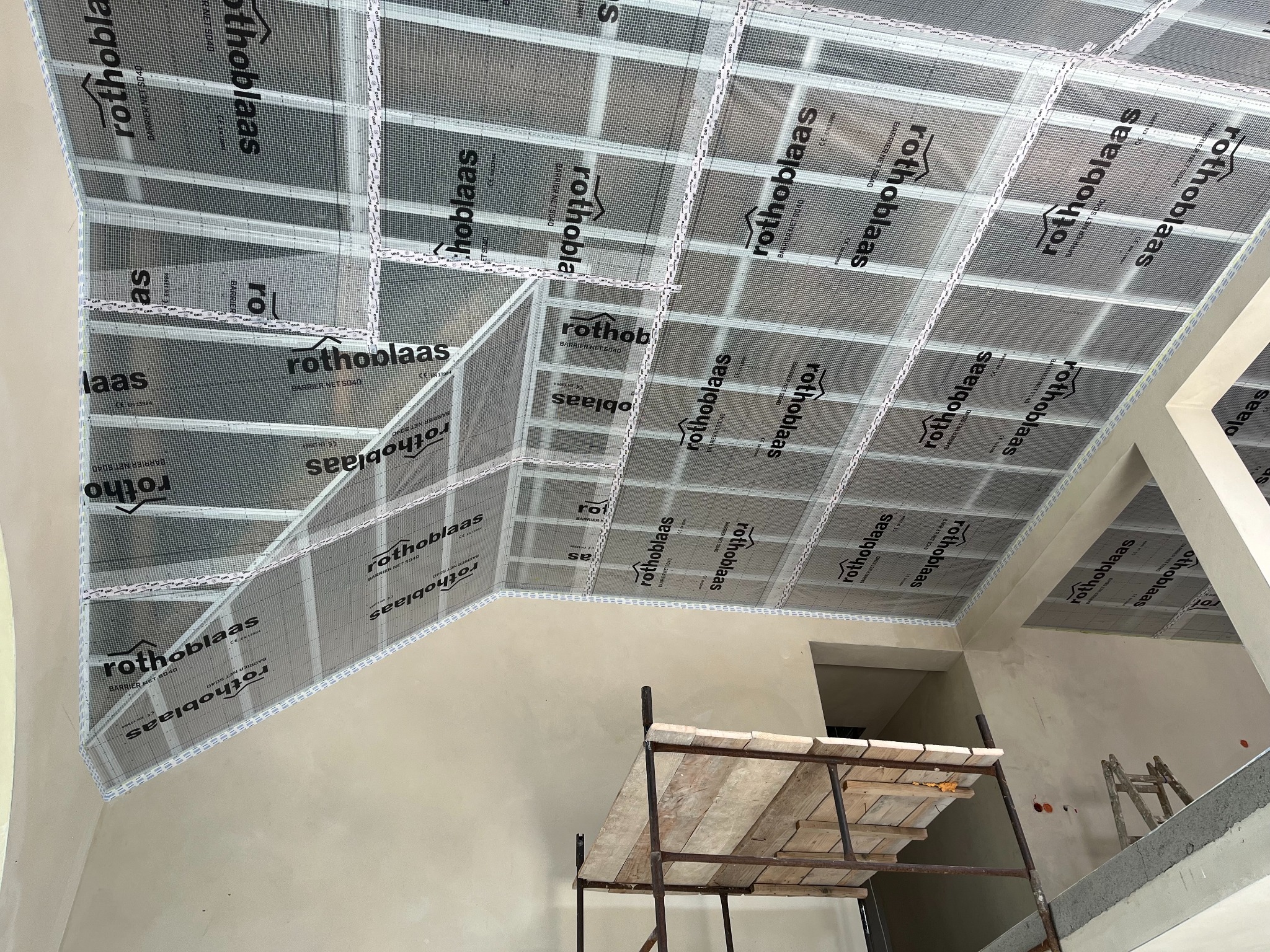 Siatka montażowa Rothoblaas na poddaszu, widok z dołu. Konstrukcja z profili i siatki, przygotowana do dalszych prac wykończeniowych. Widoczne rusztowanie.