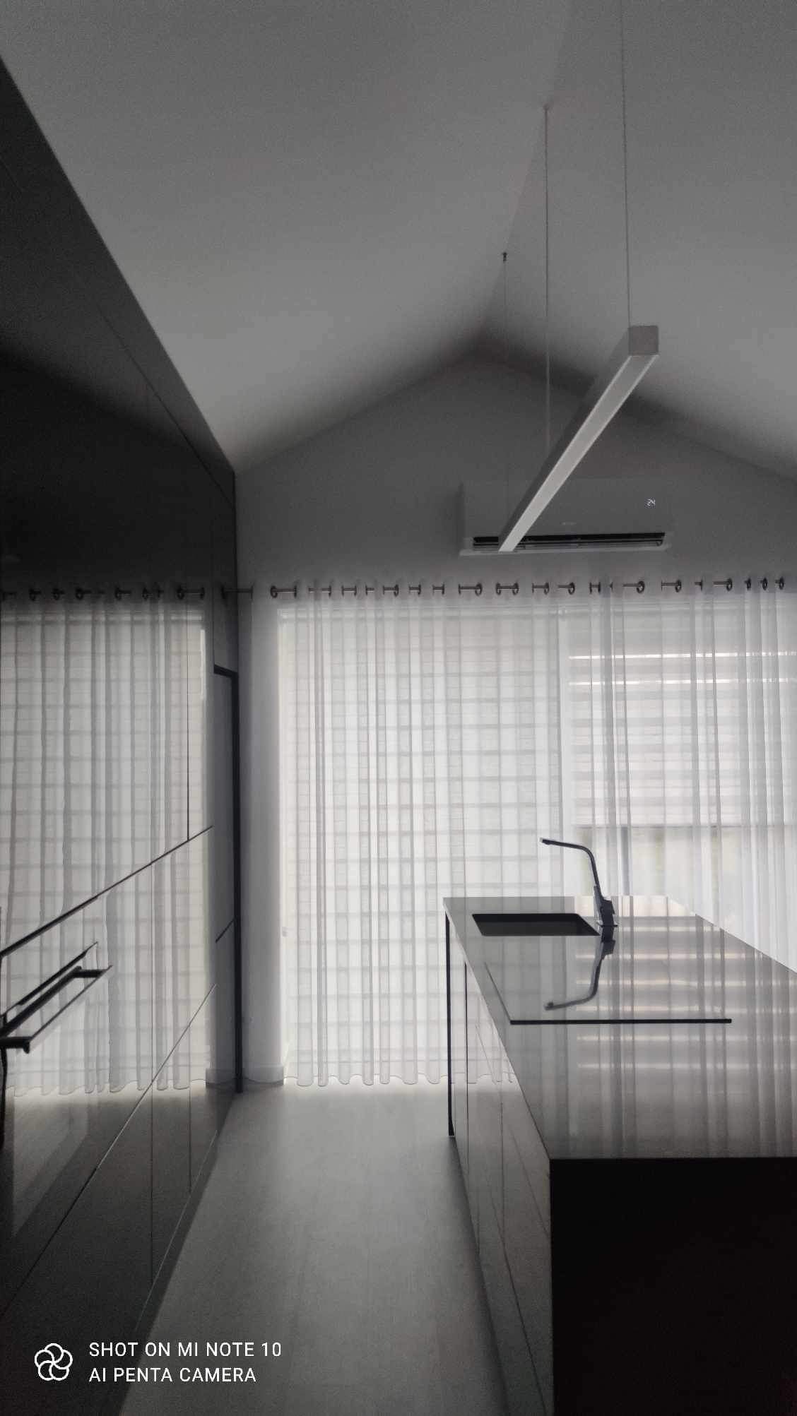 Minimalistyczna kuchnia w odcieniach szarości z czarną wyspą, oświetleniem LED i przesłoniętymi oknami.