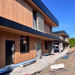 IVAN PRYVEDA - Nowoczesny dom z drewnianą elewacją i kamiennymi elementami wykończeniowymi, w trakcie prac wykończeniowych na zewnątrz budynku.
