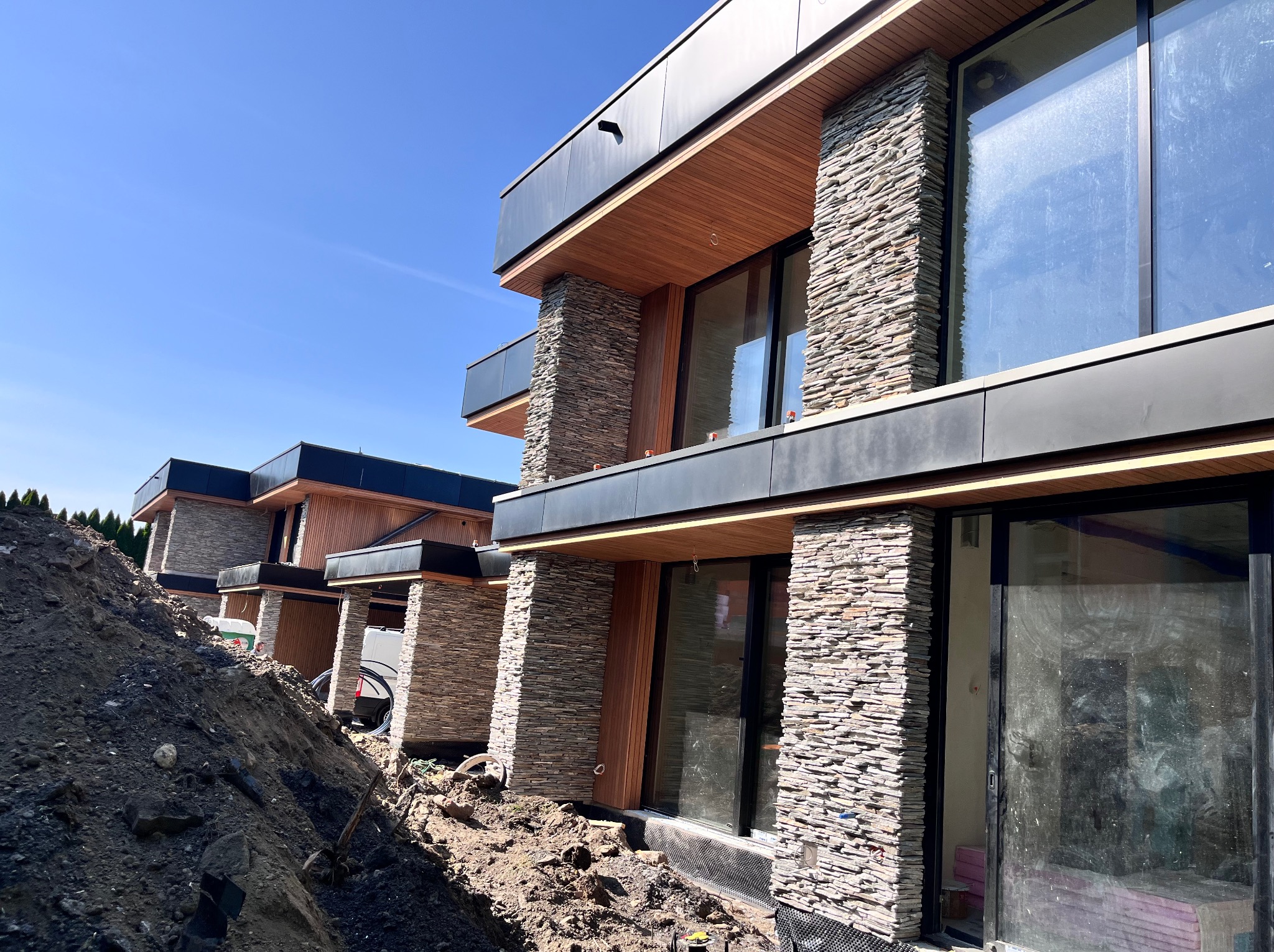 Nowoczesne domy w zabudowie szeregowej z elewacją z kamienia naturalnego i drewnianymi elementami wykończeniowymi, widoczne z poziomu gruntu.