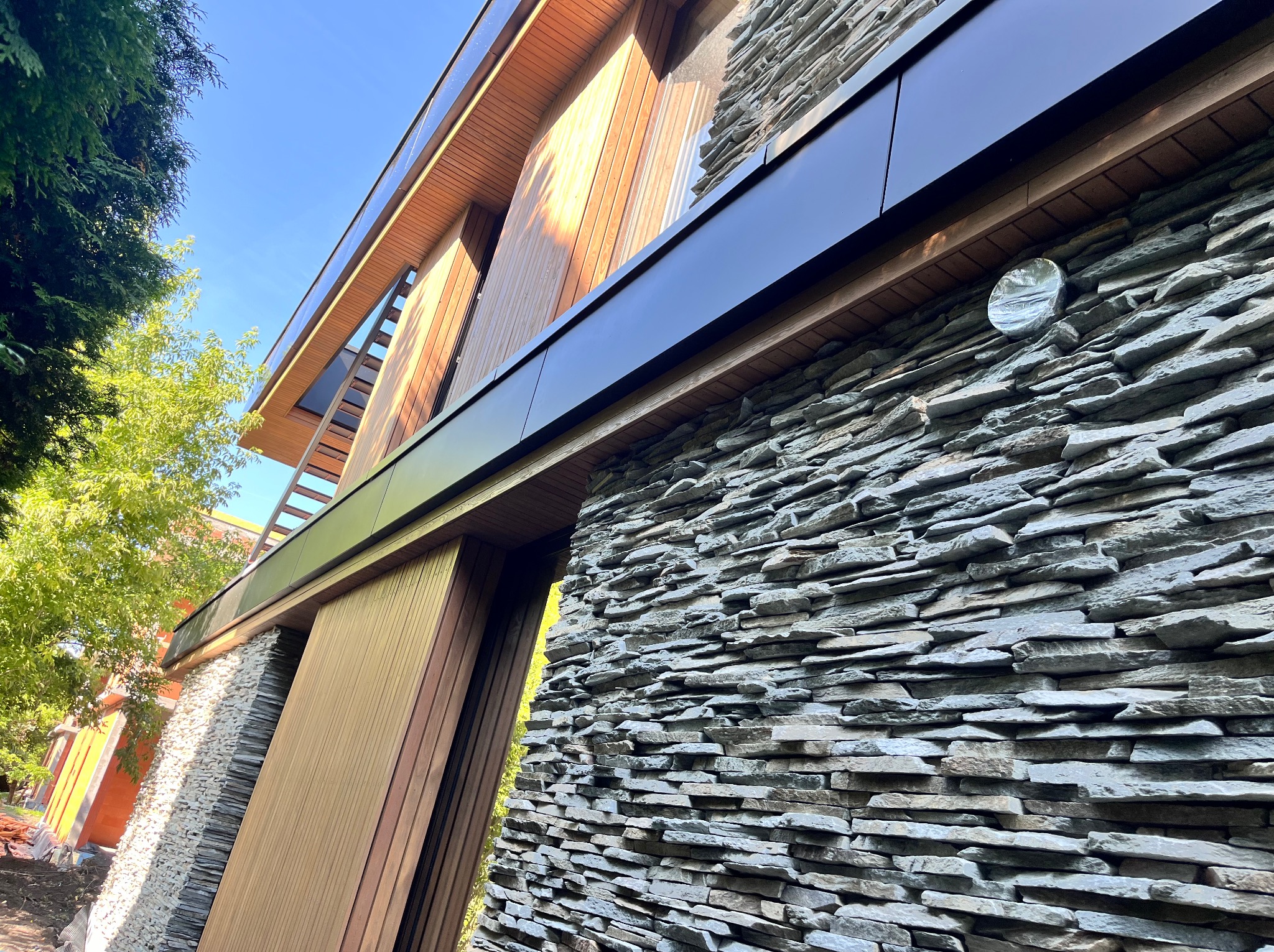 Nowoczesna elewacja budynku z kamienia łupanego i drewnianych paneli, widok z dołu, podkreślający unikalne połączenie materiałów i architekturę.
