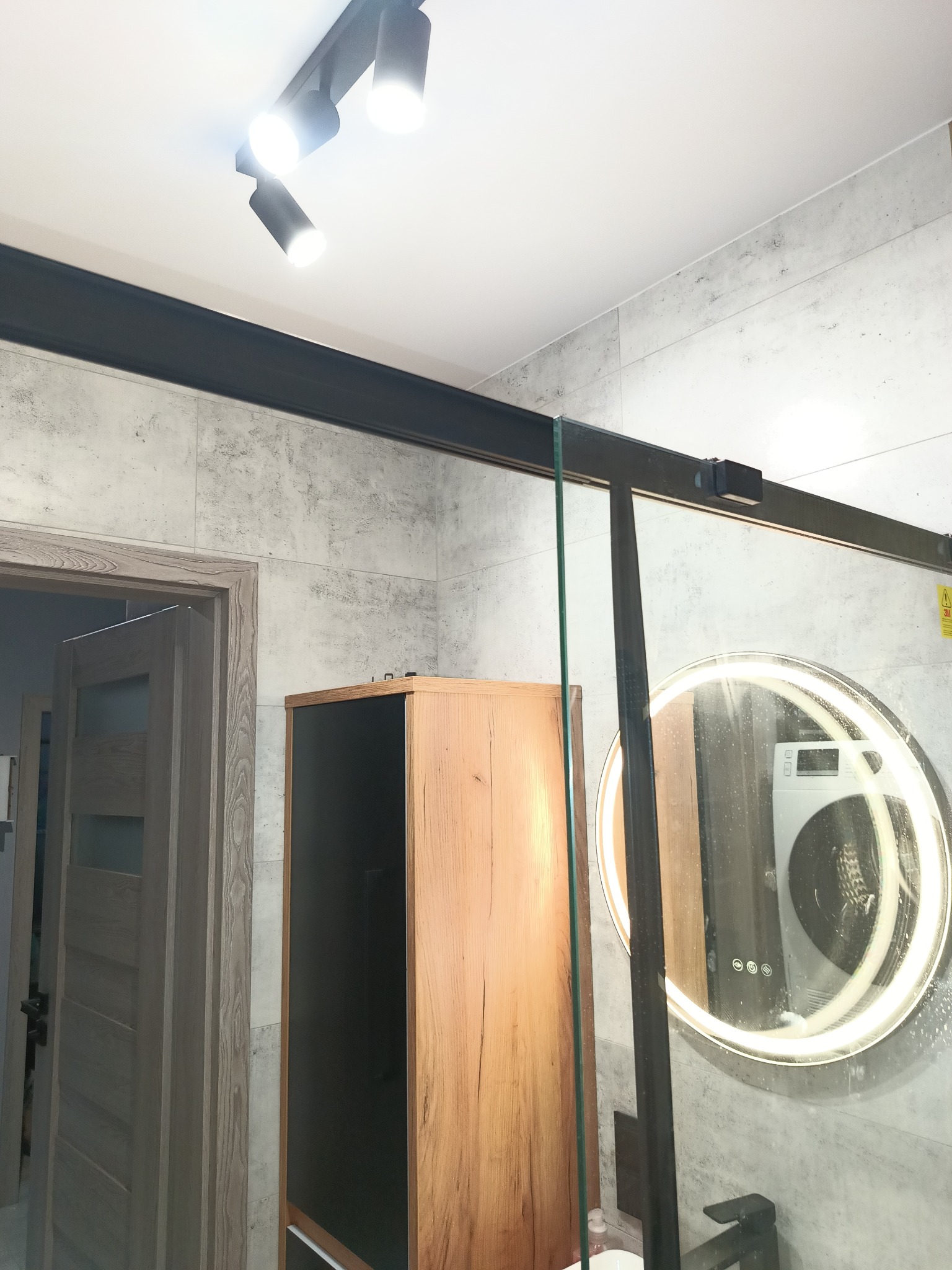 Wykończona łazienka w Łodzi z kabiną prysznicową z czarnymi profilami, okrągłym lustrem z podświetleniem LED i drewnianą szafką.