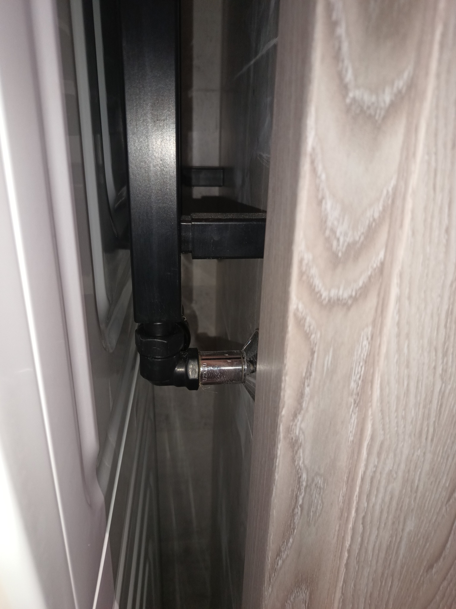 Fragment łazienki z zamontowanym czarnym grzejnikiem drabinkowym, widoczne chromowane zawory i płytki imitujące drewno na ścianie.