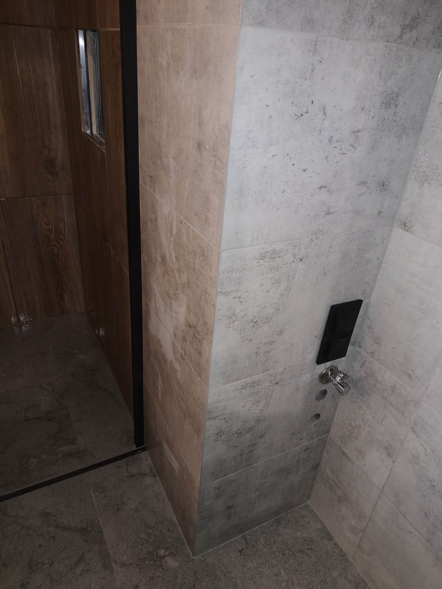 Wykończona kabina prysznicowa z szarymi i beżowymi płytkami imitującymi kamień, czarną armaturą i odpływem liniowym.