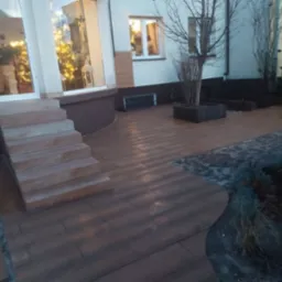 Ułożona kostka brukowa w odcieniach brązu prowadząca do schodów wejściowych domu z oknami odbijającymi świąteczne dekoracje.