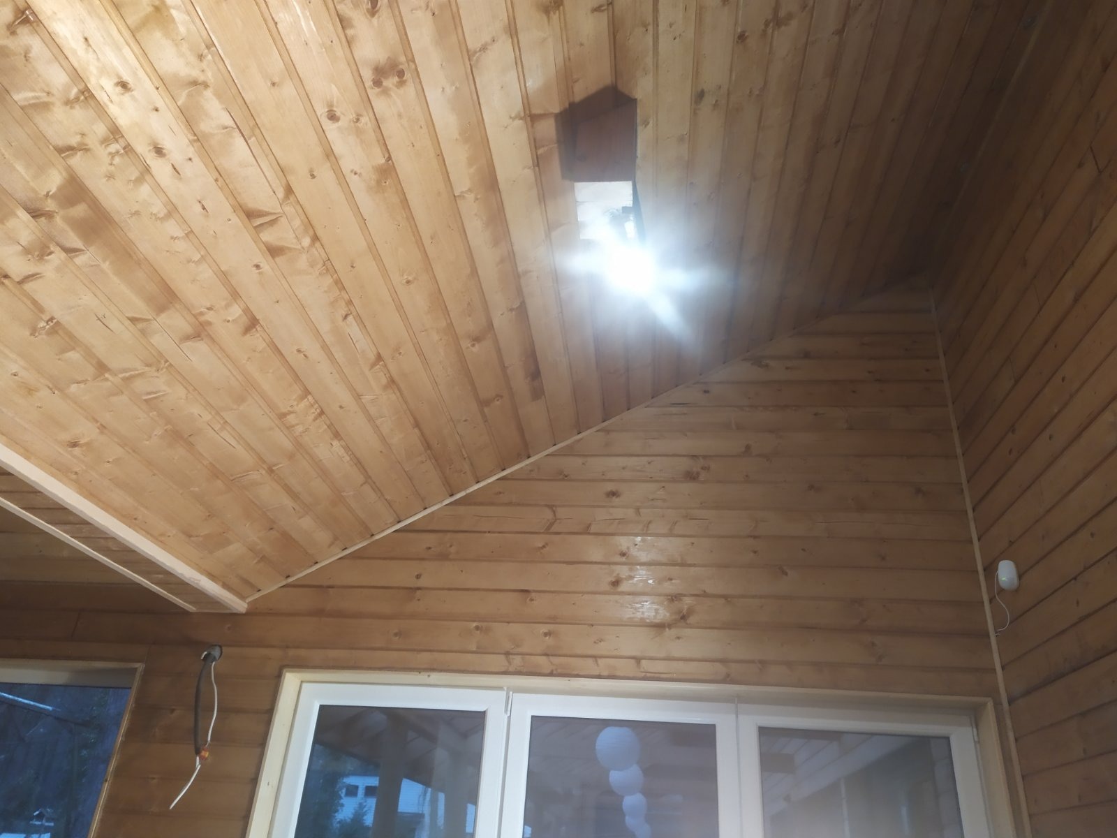 Drewniana boazeria na suficie i ścianach poddasza z oknem dachowym i widocznym oświetleniem.