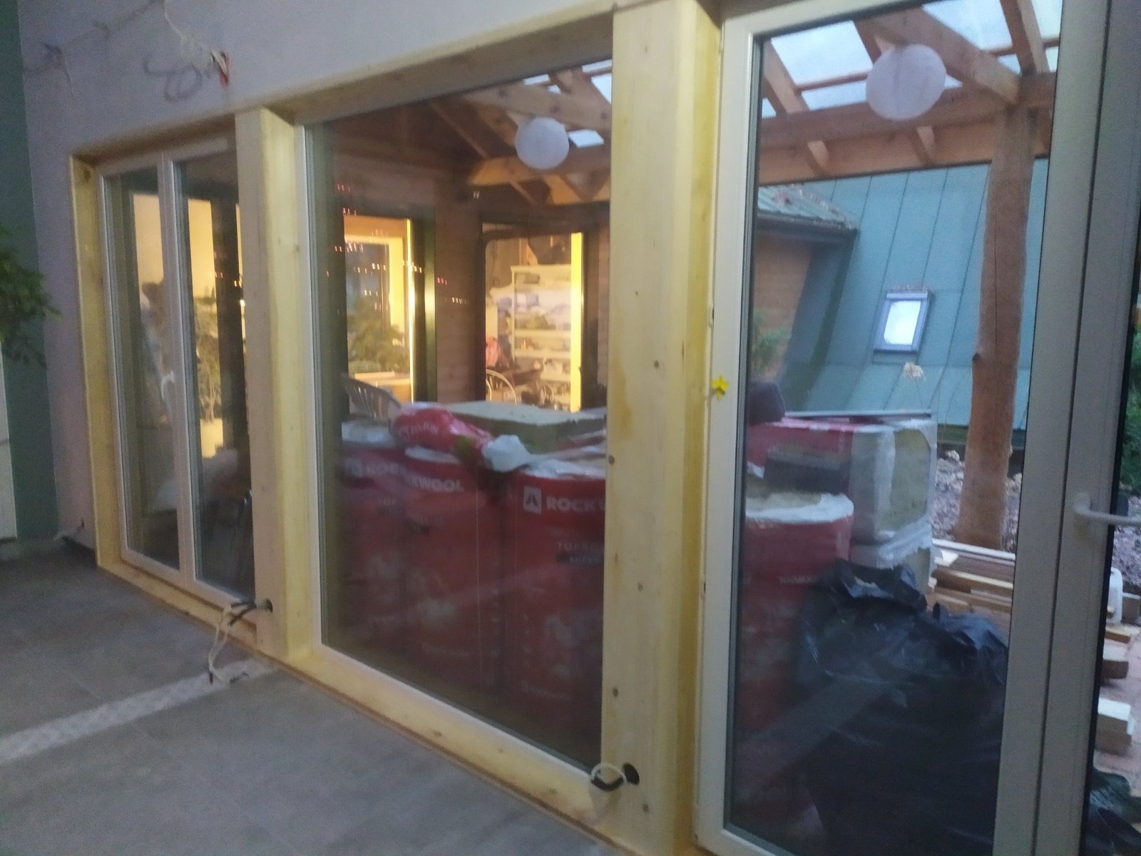 Wnętrze w trakcie wykańczania z widocznymi oknami, drewnianą konstrukcją, izolacją Rockwool i elementami wykończeniowymi na zewnątrz.