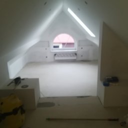 Remonty A&P - Poddasze w trakcie prac przygotowawczych do wykończenia, widoczne okno dachowe, grzejnik, narzędzia i materiały budowlane, ściany przygotowane do malowania.