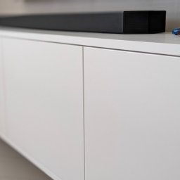 ESEN STUDIO - Biała szafka RTV z gładkimi frontami, na której stoi czarny soundbar i trzy miniaturowe modele samochodów osobowych.