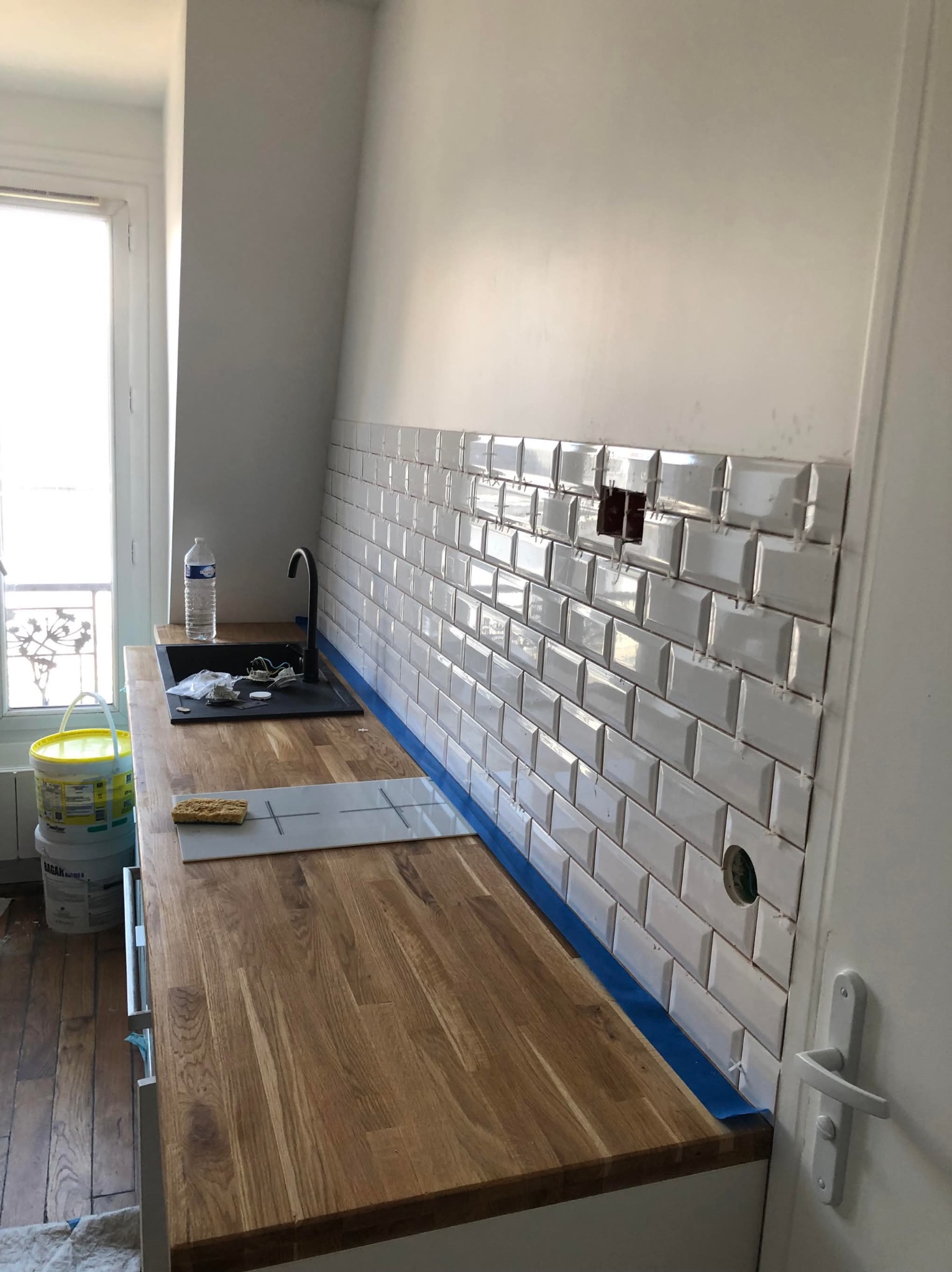 Montaż białych płytek typu metro w kuchni w Jeżowem. Widoczne narzędzia i materiały budowlane. Częściowo ułożona glazura z pozostawionymi otworami na instalacje.