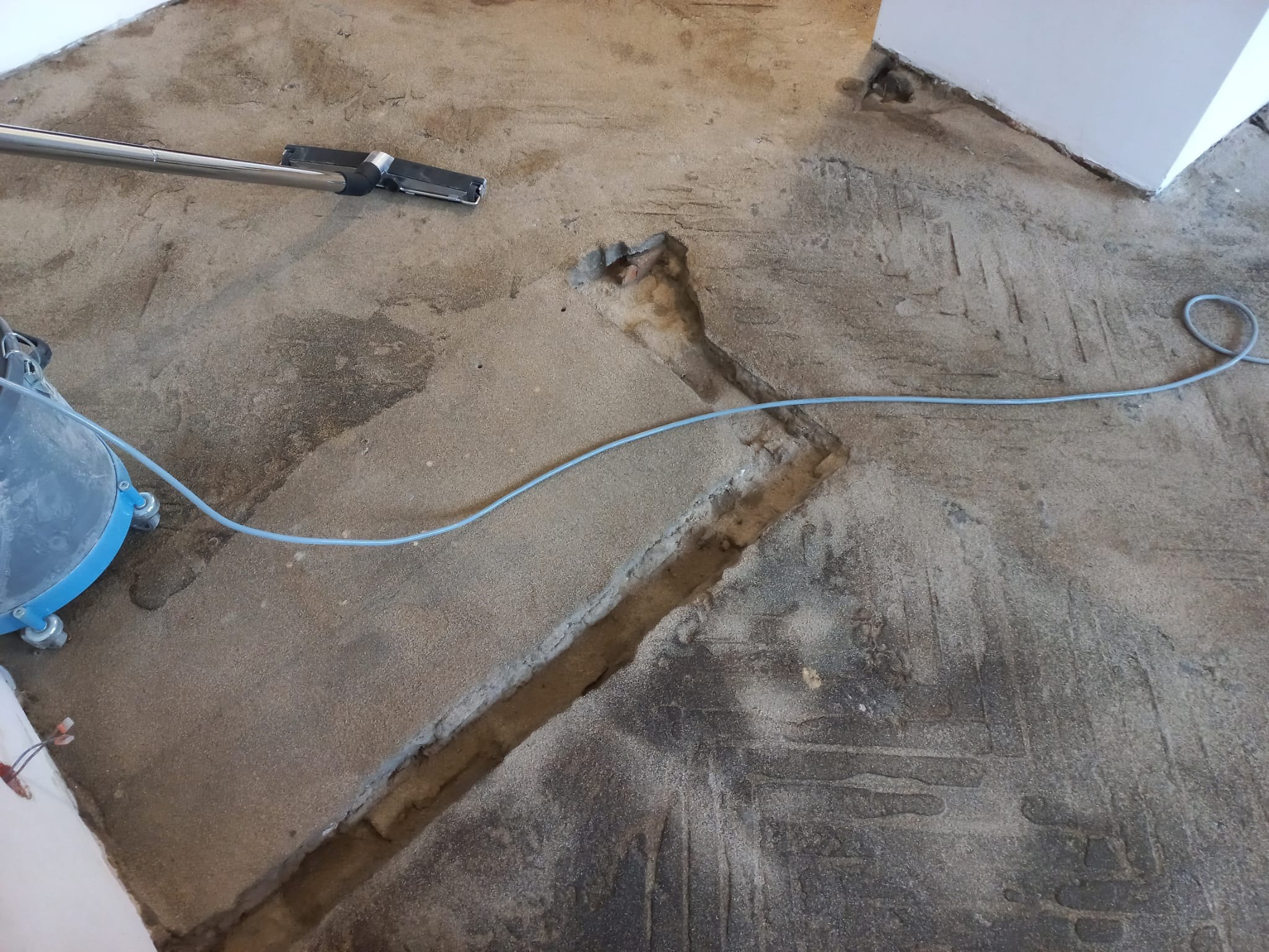 Przygotowanie podłoża w Zabrzu: widoczny fragment podłogi z wyciętymi szczelinami, pozostałości kleju po parkiecie, oraz odkurzacz przemysłowy z niebieskim zbiornikiem.