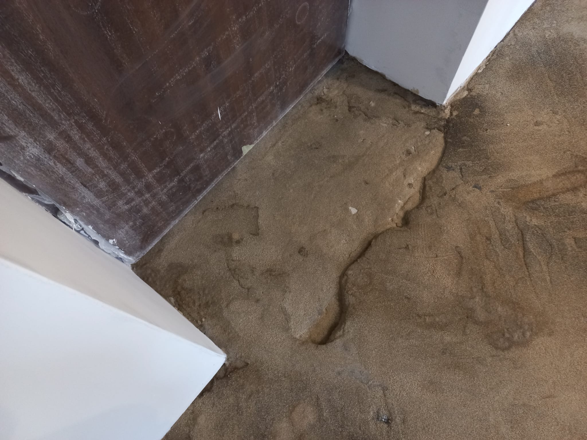 Przygotowanie podłoża pod wylewkę: wyrównana, piaskowa powierzchnia w rogu pomieszczenia, widoczne ślady po szpachlowaniu na ścianie i listwach przypodłogowych.