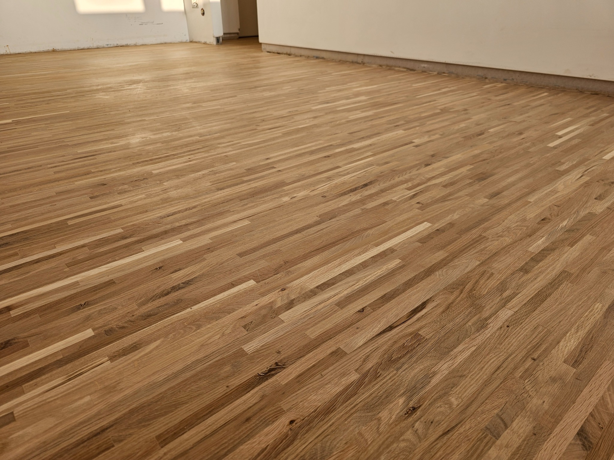 Ułożony, świeżo polakierowany parkiet w jasnym odcieniu dębu, widoczne niedoskonałości ściany i brak listew przypodłogowych.