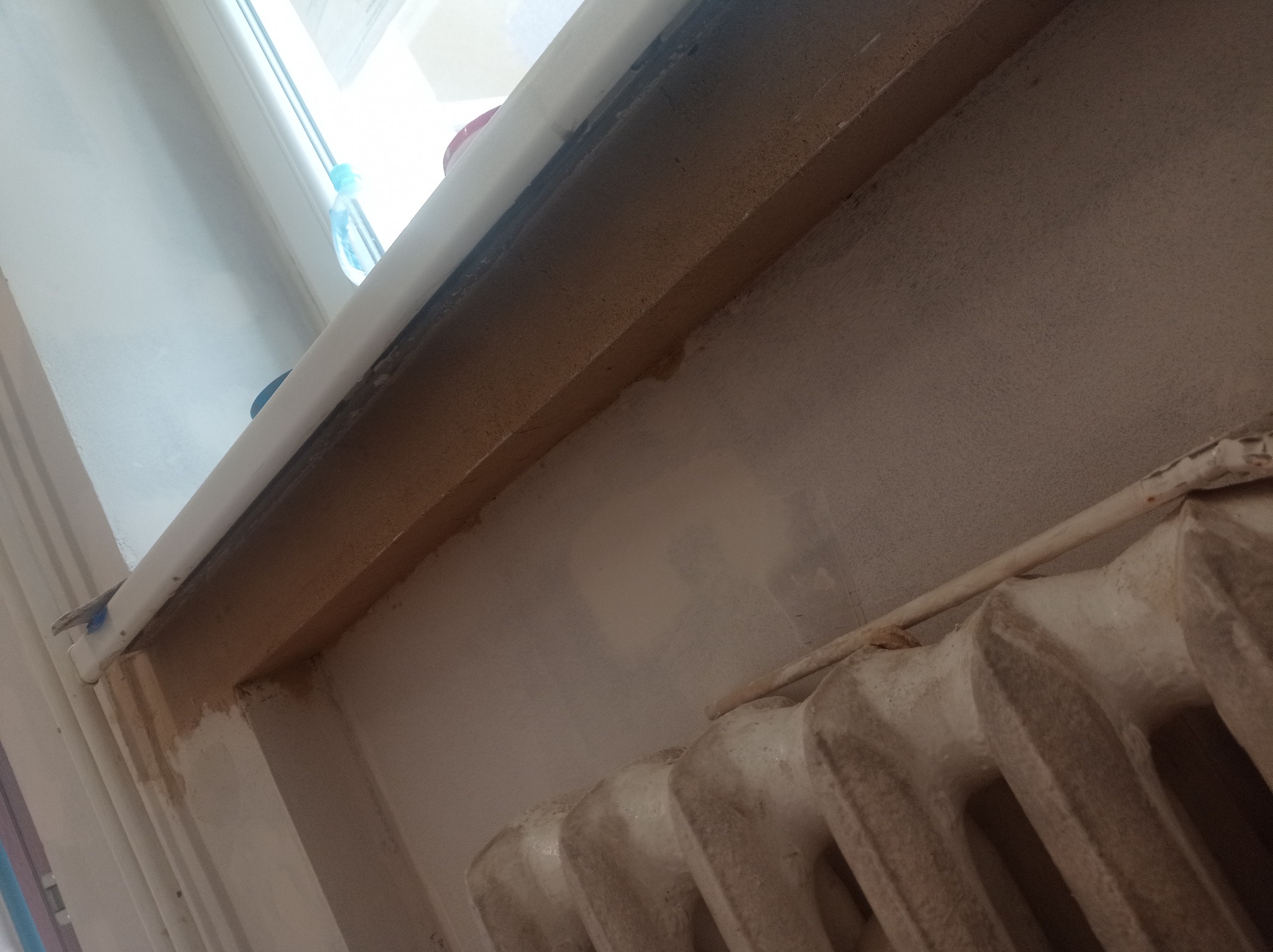 Fragment ściany z grzejnikiem żeliwnym i parapetem okiennym w trakcie przygotowywania do malowania, widoczne ślady szpachlowania.