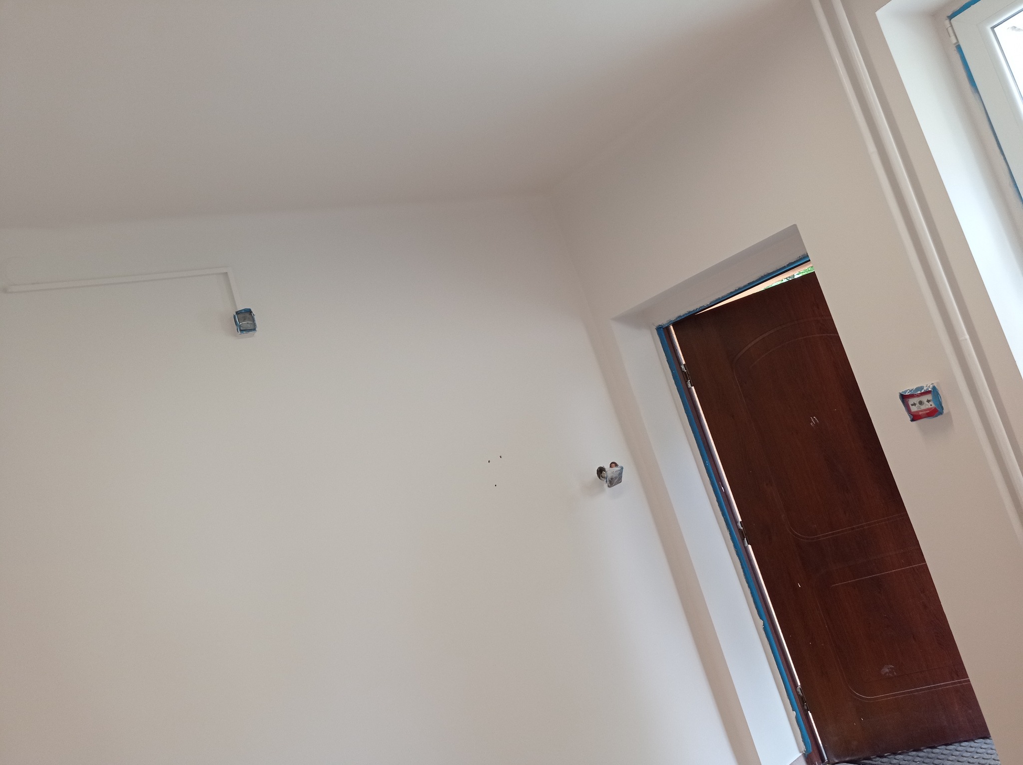 Wnętrze pokoju w Jastrzębiu-Zdroju po malowaniu ścian na biało, widoczne gniazdka elektryczne i zabezpieczone taśmą futryny drzwi.