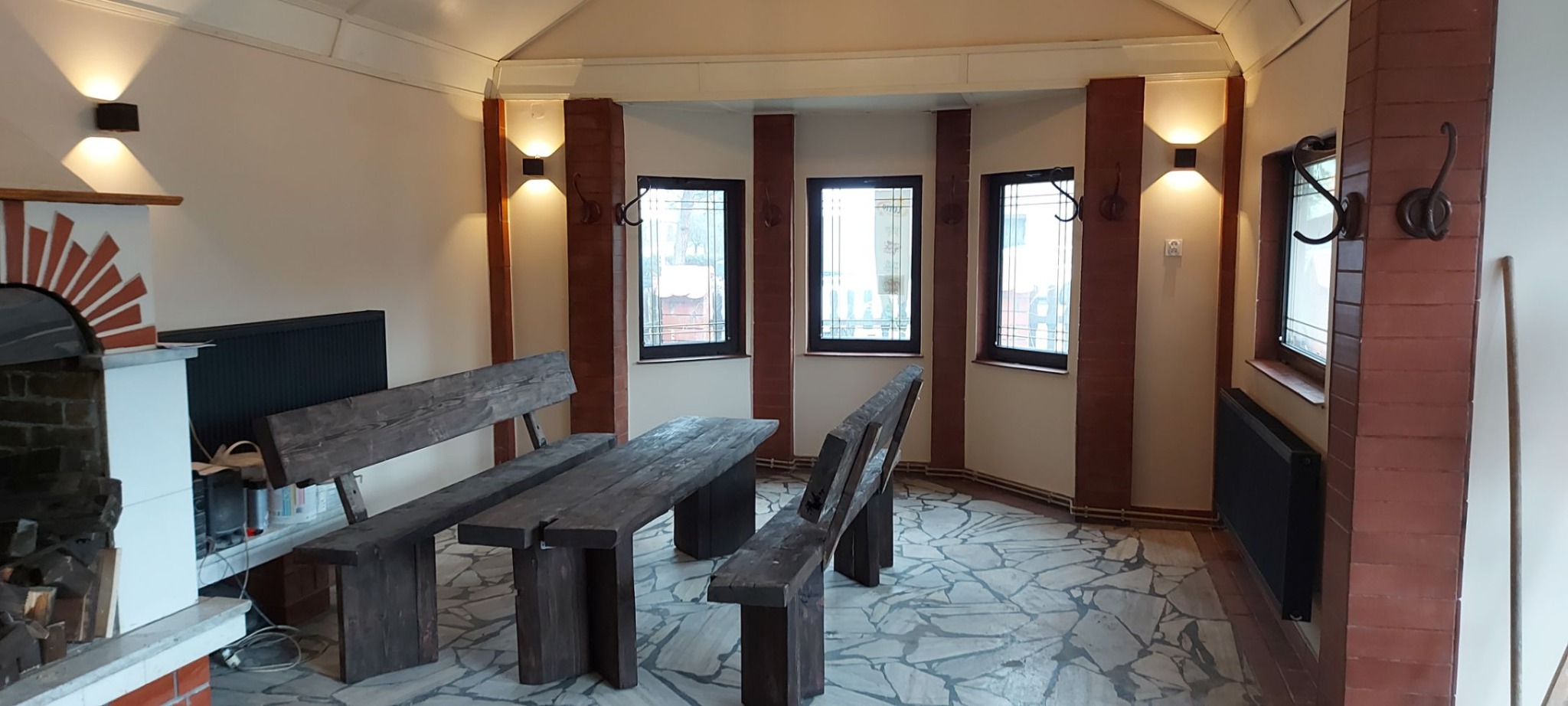 Rustykalna jadalnia z drewnianym stołem i ławkami, kamienną posadzką, ceglanymi filarami i oświetleniem ściennym.