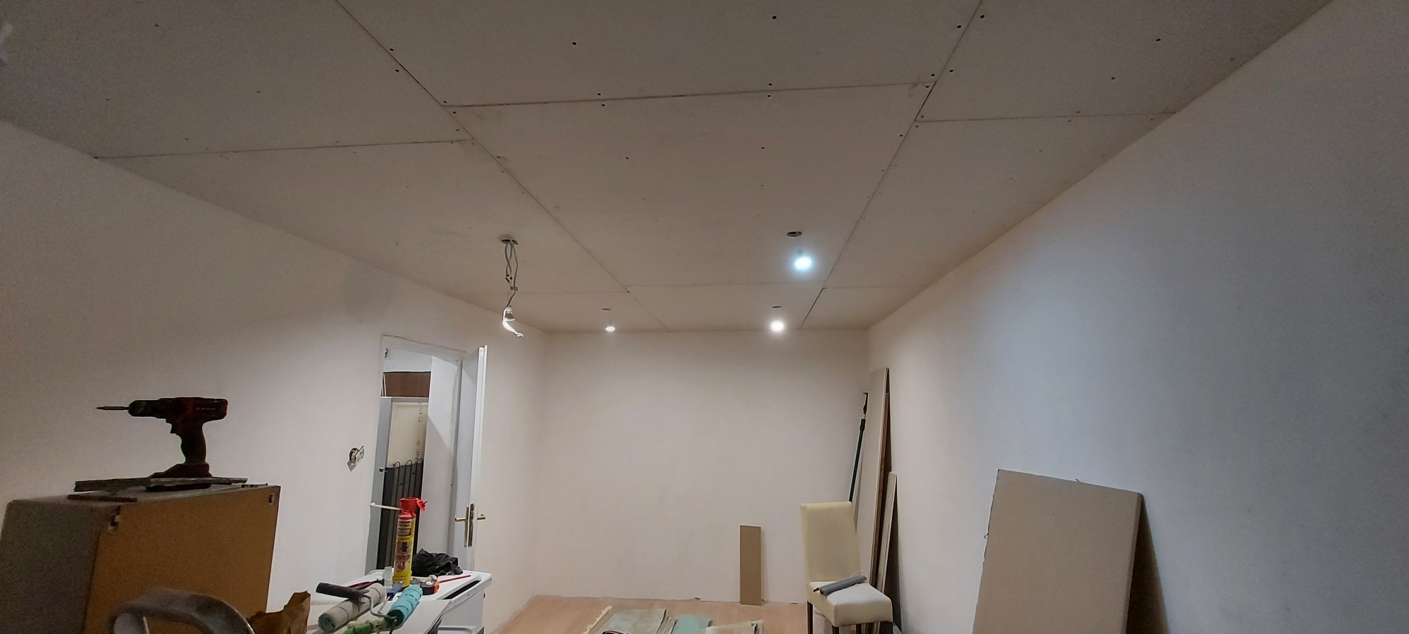 Montaż sufitu z płyt karton gips w trakcie prac, widoczne narzędzia i częściowo zamontowane płyty, z wiszącym przewodem oświetleniowym.