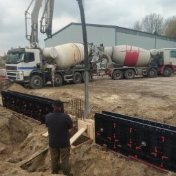 Budowa Marzeń - Wylewanie betonu do szalunków fundamentowych za pomocą pompy z betonomieszarki, widoczny pracownik w czapce obserwujący proces.