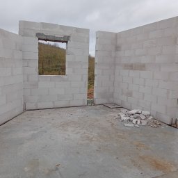 Budowa Marzeń - Wnętrze w stanie surowym otwartym z częściowo wzniesionymi ścianami z bloczków, widoczne okno z nadprożem i wystającymi prętami zbrojeniowymi z fundamentu, na posadzce resztki materiałów...