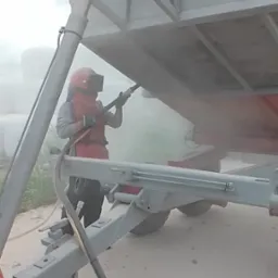 Pracownik w kombinezonie ochronnym oczyszcza strumieniem ścierniwa przyczepę rolniczą, przygotowując ją do malowania.