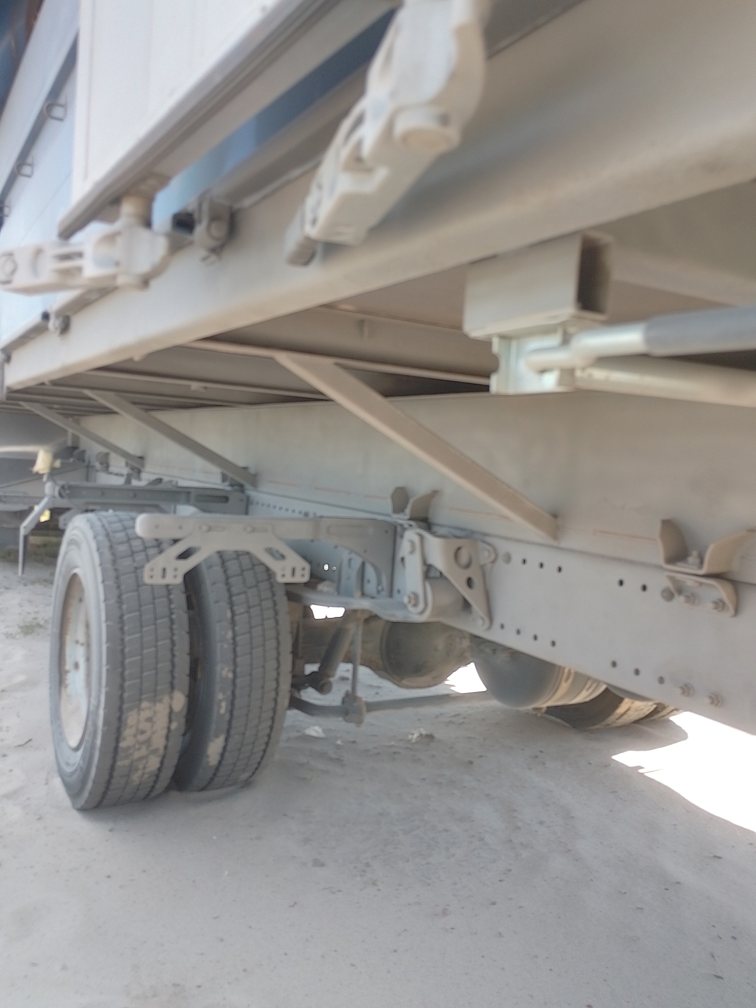 Podwozie naczepy samochodowej z widocznymi kołami i elementami konstrukcyjnymi, pokryte jednolitą, szarą powłoką.